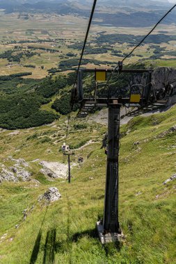 Boş kayak koltuğu yeşil yaz yamaçlarında ve kayalık dağ arazilerinde hareket ediyor. Mevsimsel turizm, dağlık tatil beldeleri veya sezon dışı dağ altyapısı için sembolik ve çok yönlü bir imaj.