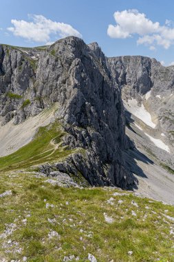 Dağların yüksek rakımlı manzarası engebeli uçurumlarda dönüyor ve küçük yürüyüşçüler görünüyor. Dramatik alp manzarası yürüyüş, macera sporları, keşif ve doğa fotoğrafçılığı için idealdir..
