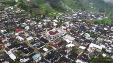 Geleneksel evleri ve merkezinde önemli bir camii olan kalabalık bir köyün havadan görünüşü. Bereketli yeşil tepeler ve teraslı tarlalar resim gibi bir manzara yaratır. Dieng Platosu.