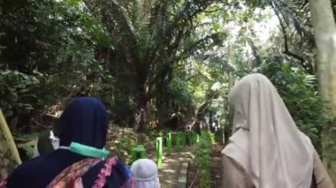 Yeşilliklerle çevrili orman yolunda yürüyen tesettürlü bir grup kadın. Yol, yoğun bir tropikal çevreye giden yeşil noktalarla işaretlenmiş..