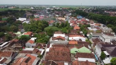 Yeşillik ve tarlalarla çevrili kırmızı kiremitli evlerin yoğun düzenlendiği bir yerleşim alanının havadan görünüşü.