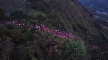 Şafak vakti geniş bir grup insan, teraslı tarlaları ve uzak dağları olan bir vadiye bakan bir yamaçta toplandı. Sahne, bir topluluk ve doğa duygusunu yakalar. Dieng Platosu.