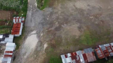 Toprak bir yol, metal çatılı küçük evler ve yeşil çimen parçalarını gösteren kırsal bir bölgenin havadan görüntüsü. Dieng Platosu, Endonezya.