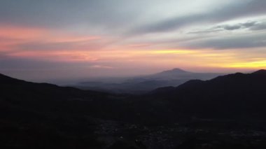 Güneş doğarken gökyüzünde canlı renklerle dağların nefes kesici manzarası. Siluetli zirveler doğanın güzelliğini gösteren dramatik bir manzara yaratır. Dieng Platosu, Endonezya.