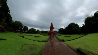 Bajang Ratu Tapınağı Majapahit döneminin bir kalıntısıdır. Merkezinde kırmızı tuğlalı bir yapı bulunan yemyeşil bir bahçenin panoramik görüntüsü. Bahçe, düzgünce düzenlenmiş çitlerle ve yapıya giden yollarla iyi korunuyor..