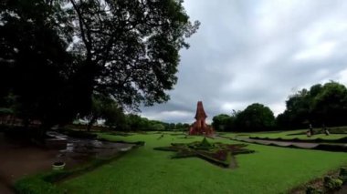 Bajang Ratu Tapınağı Majapahit döneminin bir kalıntısıdır. Manikürlü çimlerin olduğu yemyeşil bir arazi ve arka planda tarihi bir yapı. Gökyüzü bulutlu, sakin bir atmosfer yaratıyor..