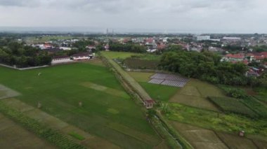 Bulutlu bir gökyüzünün altında yeşil tarlaları, evleri ve ağaçları olan kırsal bir manzara..