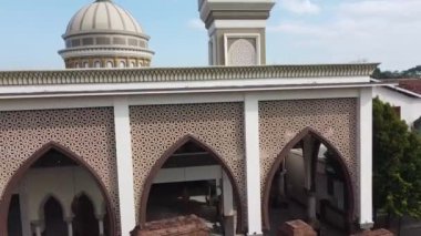 Büyük bir kubbesi ve iki minaresi olan bir caminin havadan görünüşü. Camide cephesinde ve kemerli camlarında karmaşık geometrik desenler var. Gökyüzü açık ve mavi.