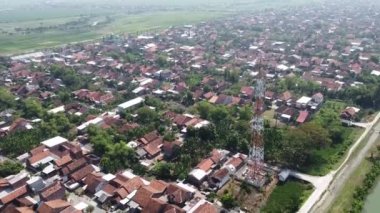 Kırmızı kiremitli çatıları ve iletişim kulesi olan yoğun nüfuslu bir yerleşim bölgesinin havadan görüntüsü. Bölge yeşil tarlalar ve ağaçlarla çevrili..