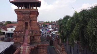 Kırmızı çatılı binaları ve işlek bir sokak marketi olan kentsel bir bölgedeki geleneksel tuğla kule manzarası. Menara Kudus.