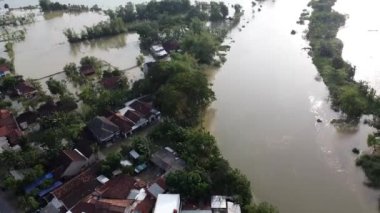Sel basmış yerleşim alanının havadan görüntüsü kısmen sular altında kalmış evler. Sel suları sular altında kalmış caddeler ve çevreleyen yeşillikler var. Görüntünün sağ tarafında bir köprü görünür..