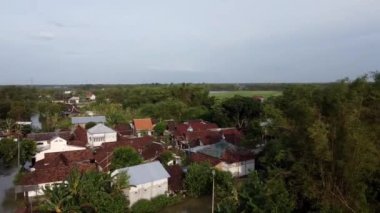 Yeşillik ve ağaçlarla çevrili geleneksel evleri olan kırsal bir köyün havadan görünüşü.