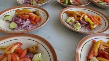Beyaz bir yüzeye dizilmiş soğan, domates, limon ve biber de dahil olmak üzere birkaç tabak dilimlenmiş sebze..