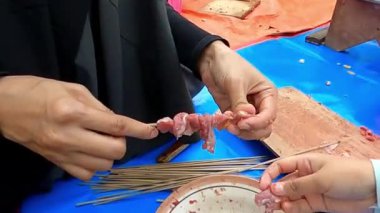 Ahşap bir sopayla çiğ et parçalarını şişleyerek ızgara yapmaya hazırlanan biri. Başka biri de şişi tutarak yardımcı oluyor..