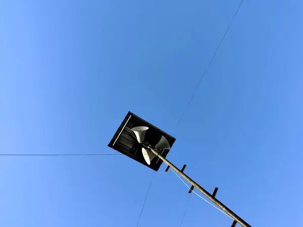 stock image Loudspeaker in a mosque. A low-angle view of a loudspeaker mounted on a pole against a clear blue sky. The speaker is white and has a square black housing, with power lines extending from the pole.