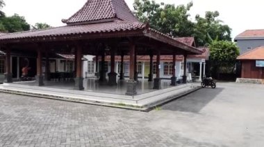 Trowulan Sub Bölge Ofisi. Döşeme çatılı ve ahşap sütunlu geleneksel bir Cava pavyonu, çevresindeki binalar ve yeşilliklerle çevrili bir avluda yer alıyor..
