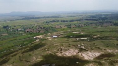 Kesongo çamur volkanı bölgesi, Blora, Endonezya. Yeşil tarlaları ve çorak arazileri olan kırsal bir arazinin havadan görünüşü. Bölgeye seyrek ağaçlar ve küçük yapılar saçılmış..