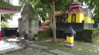 Sarı binası ve ağaçlarla çevrili taş yapıları olan küçük bir tapınak kompleksi. Raden Wijaya, Mojokerto, Doğu Java, Endonezya