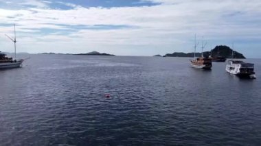 Manjarite Sahili, Labuan Bajo, Endonezya: Durgun sularda demirli birkaç teknesi olan sakin bir deniz manzarası, parçalı bulutlu bir gökyüzünün altında görünen adalar.