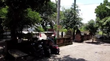 Mojokerto, Endonezya - 226 2022: Park halindeki motosikletli, ağaçlı ve birkaç kişi ayakta duran küçük bir açık hava alanı. Bölgede tuğla yapılar ve banklar ile kırsal bir his var. Trowulan.