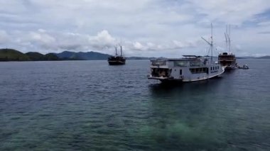 Kelor Adası, Labuan Bajo, Endonezya: Arkasında dağlar olan sakin bir denize demirlemiş iki tekne bulutlu bir gökyüzünün altında.