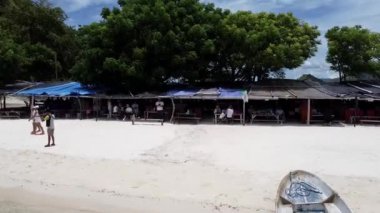 Labuan Bajo, Endonezya - 03 08 2023: Kapalı muşambalarla kaplı derme çatma tezgahların altında yürüyen ve altında oturan insanların olduğu bir sahil pazarı.