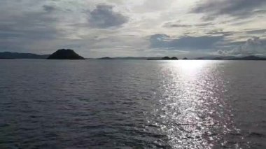 Sakin suları yansıtan sakin bir deniz manzarası. Bulutlu bir gökyüzünün altındaki uzak adalar. Sahne, rahatlama ve seyahat temaları için ideal olan doğanın sükunetini yakalıyor..