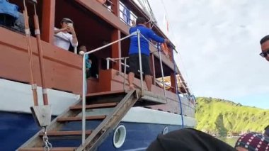 Labuan Bajo, Endonezya - 03092023: Bir grup Endonezyalı merdivenli ahşap bir tekneye biniyor. Bazı bireyler günlük giysiler giyiyor ve bir kişi el sallıyor..