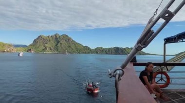 Labuan Bajo, Endonezya - 03092023: rıhtımdan manzaralı bir manzara. Küçük bir balıkçı teknesi rıhtıma yaklaşırken Endonezyalı bir kadın kenarda oturmuş manzaranın tadını çıkarıyor..