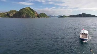 Sakin sulara demir atmış, berrak mavi gökyüzünün altında ıssız, yemyeşil adalarla çevrili, sakin bir deniz manzarası. Manzara sakin bir kıyı ortamını gözler önüne seriyor.