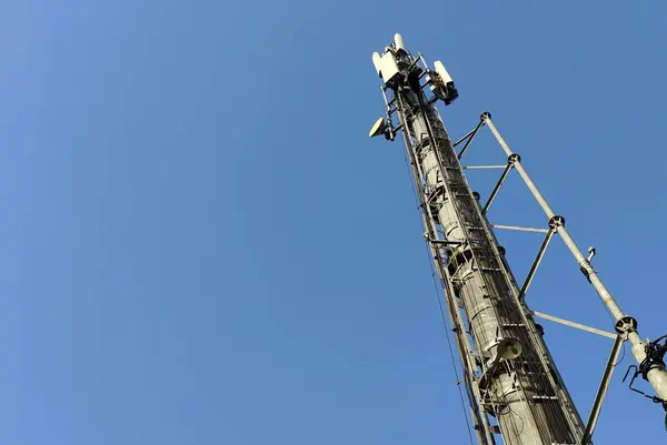 Yüksek bir telekomünikasyon kulesi, açık mavi gökyüzüne karşı, yapısına anten ve ekipman monte edilmiş..