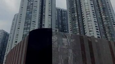 Bulutlu mavi gökyüzüne karşı modern gökdelenlerin manzarası. Mimaride cam ve beton karışımı sergilenen kentsel gelişim yer alıyor..