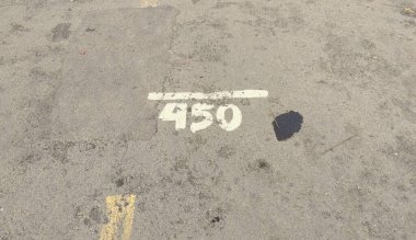 450 numaralı beyaz boyalı beton yüzeyi ve yakınlarda koyu bir lekesi olan yakın plan bir görüntü. Toprak yıpranmış görünüyor, biraz toprak ve döküntü var..