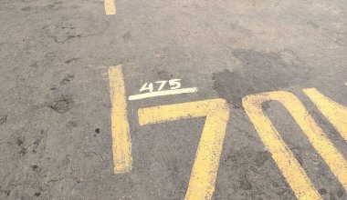 Park yeri yüzeyinin yakın çekim görüntüsü üzerinde 475 yazan sarı bir çizgi gösteriyor. Asfalt yıpranmış ve biraz kir ve leke var. Bu da ağır kullanımı gösteriyor..