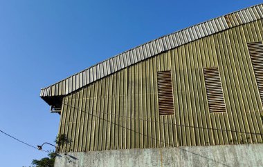 Açık mavi gökyüzüne karşı kıvrımlı çatılı büyük, yıpranmış bir ahırı yakından görmek. Ahırda dikey tahta çıtalar ve birkaç yatay havalandırma var..