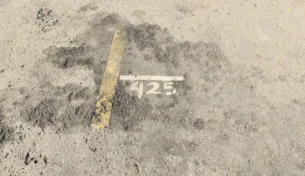 Kirli asfalt bir yüzey üzerinde '425' yazan soluk bir park yeri numarası..