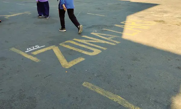 Üzerinde 'ZONA LARI' (çalışma bölgesi) yazan sarı işaretlerle beton bir yüzeyde yürüyen bir kişi. Arkaplan biraz bulanık, metni ve bireyi vurguluyor.