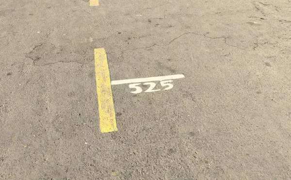 stock image A close-up view of a parking lot surface showing a yellow line and the number 525 painted in white. The asphalt is cracked and worn, indicating use over time.