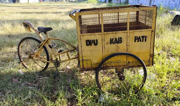 Üzerinde metal ağ tasarımı olan büyük bir kargo kutusu olan eski sarı bir bisiklet. Kargo kutusunda 'DPU KAB PATI' yazıyor. Çeviri: Pati Regency Bayındırlık Departmanı.