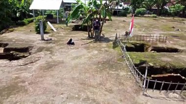 Kerto Mataram İslami Sitesi, Yogyakarta, Endonezya. Endonezya 'da kırsal bir alanda muz ağaçlarının yanında duran bir adamın havadan görünüşü, yanında bir bayrak ve sırt çantasıyla..