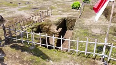 Kerto Mataram İslami Sitesi, Yogyakarta, Endonezya. Ahşap bir çitle çevrili, açıkta kalmış harabelerin bulunduğu bir arkeolojik alanın havadan görüntüsü. Toprak yosun ve otla kaplı..