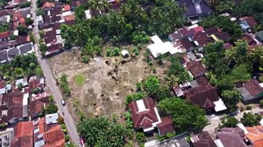 Kerto Mataram İslami Sitesi, Yogyakarta, Endonezya. Yeşilliklerle çevrili boş arazi ve evlerin karışımının yer aldığı bir yerleşim alanının havadan görünüşü.