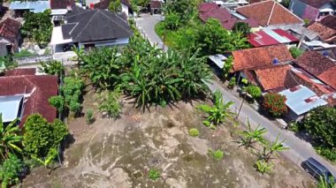 Kerto Mataram İslami Sitesi, Yogyakarta, Endonezya. Muz ağaçları ve diğer bitkiler de dahil olmak üzere yeşilliklerle çevrili kırmızı çatılı evlerin bulunduğu bir yerleşim alanının havadan görünüşü.