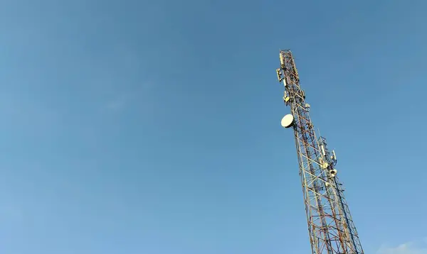Uzun bir telekomünikasyon kulesi, açık mavi gökyüzüne karşı, çeşitli antenler ve yapısına monte edilmiş tabaklarla..