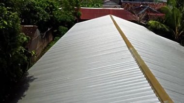 Pleret Arkeolojik Sitesi, Yogyakarta. Güneş ışığını yansıtan kıvrımlı metal bir çatının yakın çekim görüntüsü. Çatı eğimli ve paralel çıkıntılar ve vadiler serisini gösteriyor.