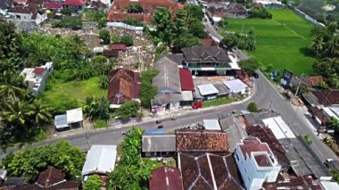 Pleret Arkeolojik Sitesi, Yogyakarta. Geleneksel evler, yeşil tarlalar ve palmiye ağaçlarının bulunduğu yerleşim alanının havadan görünüşü. Olay yerinde araçlı bir yol var.