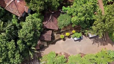 Joyokusumo 'nun mezarı, Pati Dağı, Semarang, Endonezya. Ağaçlarla çevrili, ağaçlarla çevrili ve park halindeki bir arabayla çiçek açan geleneksel evlerin bulunduğu yemyeşil bir manzaranın havadan görüntüsü.