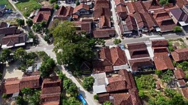 Yeşil ve dolambaçlı yollarla çevrili kırmızı kiremitli çatıları olan geleneksel bir köyün hava manzarası. Yerleşim ve ortak alanların bir karışımını gösteriyor. Pati, Java, Endonezya