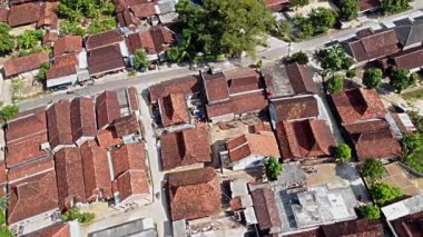 Yeşil ve dolambaçlı yollarla çevrili kırmızı kiremitli çatıları olan geleneksel bir köyün hava manzarası. Yerleşim yeri ve ortak alanların karışımını gösteriyor. Pati, Java, Endonezya.