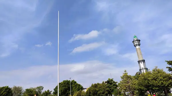 Cami kulesinin yanındaki bayrak direğinin alçak açılı görüntüsü ince bulutlu mavi gökyüzüne karşı..